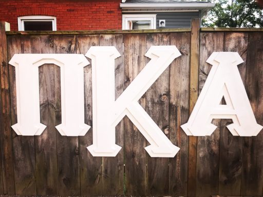 White Greek letters "ΠΚΑ" on a wooden fence.