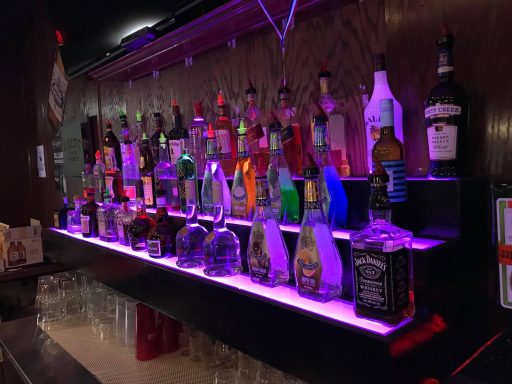 A colorful display of liquor bottles illuminated with purple light on a bar shelf.