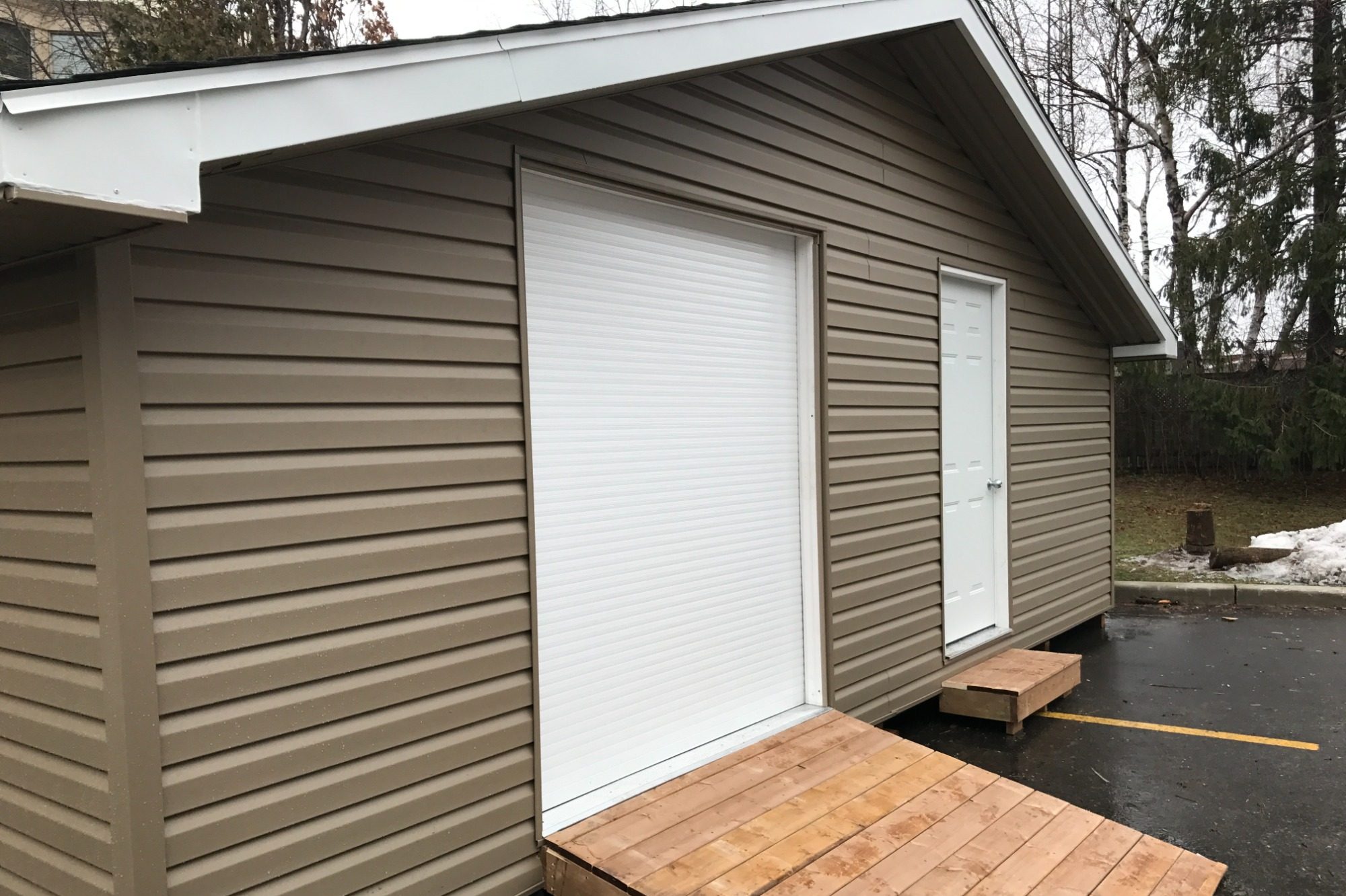 Brown wooden building with a white door and a blank window covering, situated outdoors.