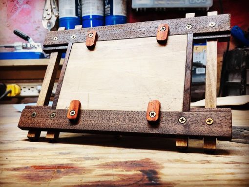 Wooden easel with a blank canvas secured by orange clamps, set on a workbench.
