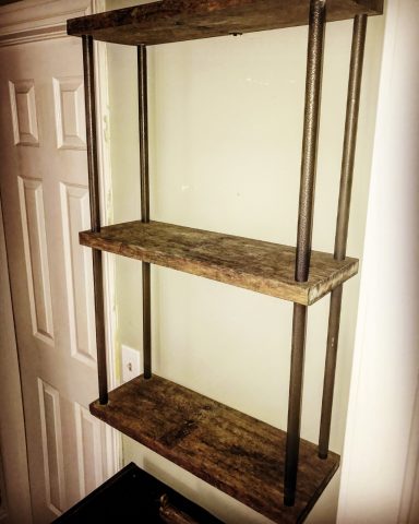 Three-tier wooden shelf with metal supports against a wall.
