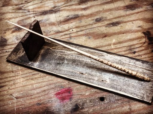 A wooden stick resting on a flat wooden surface with a small support block.