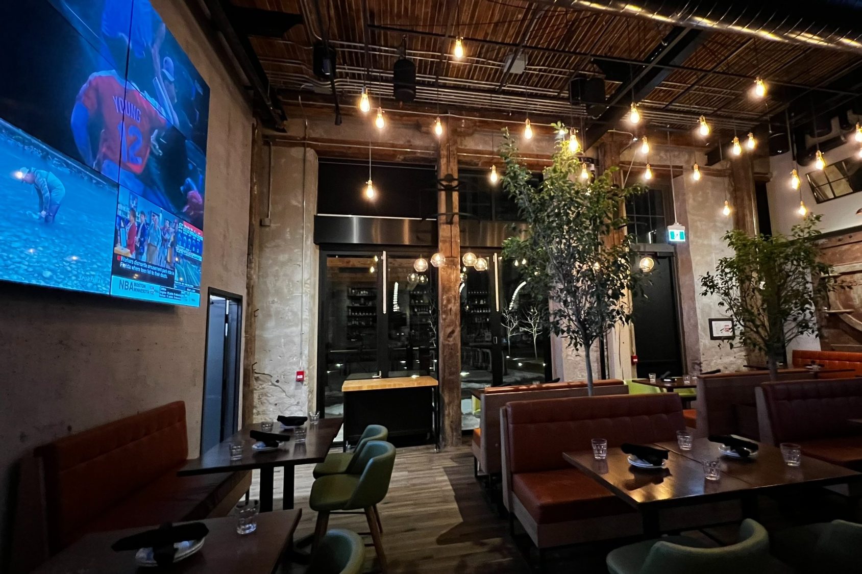 Modern restaurant interior with warm lighting, wooden beams, and large screen.