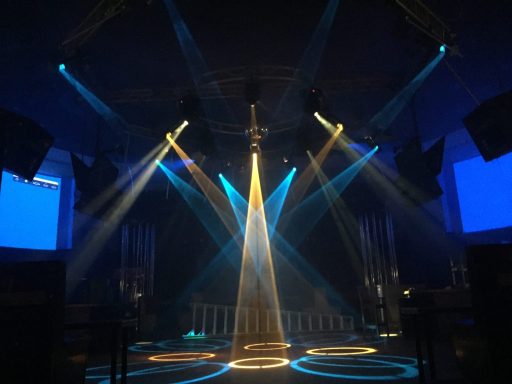 Colorful stage lights illuminate a nightclub setting with beams and patterns.