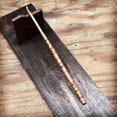A wooden stick with engraved markings resting on a dark wooden surface.