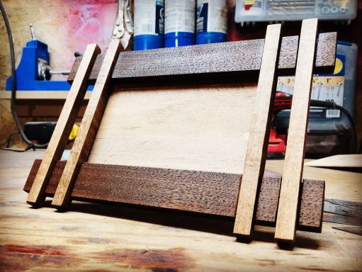 A wooden photo frame with dark and light wood accents on a workshop table.