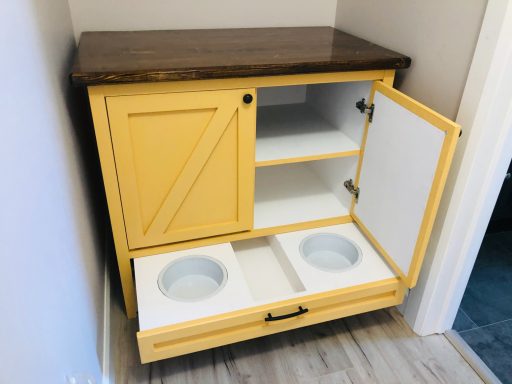 A yellow cabinet with a wooden top, featuring two bowls and shelves inside.