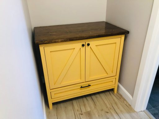 Yellow cabinet with a dark wooden top, featuring two doors and a drawer.