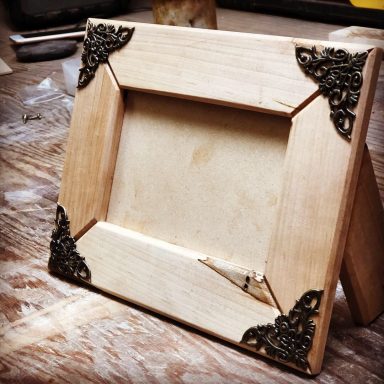 Wooden photo frame with decorative metal corners, designed to stand upright.
