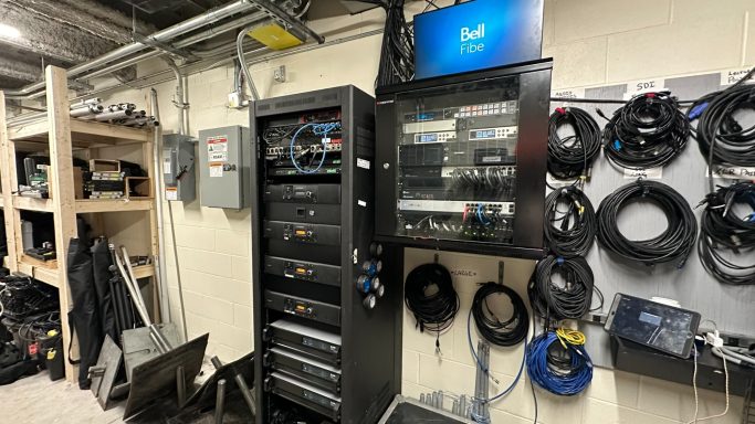 Rack of audio-visual equipment with cables organized on a wall in a tech setup area.