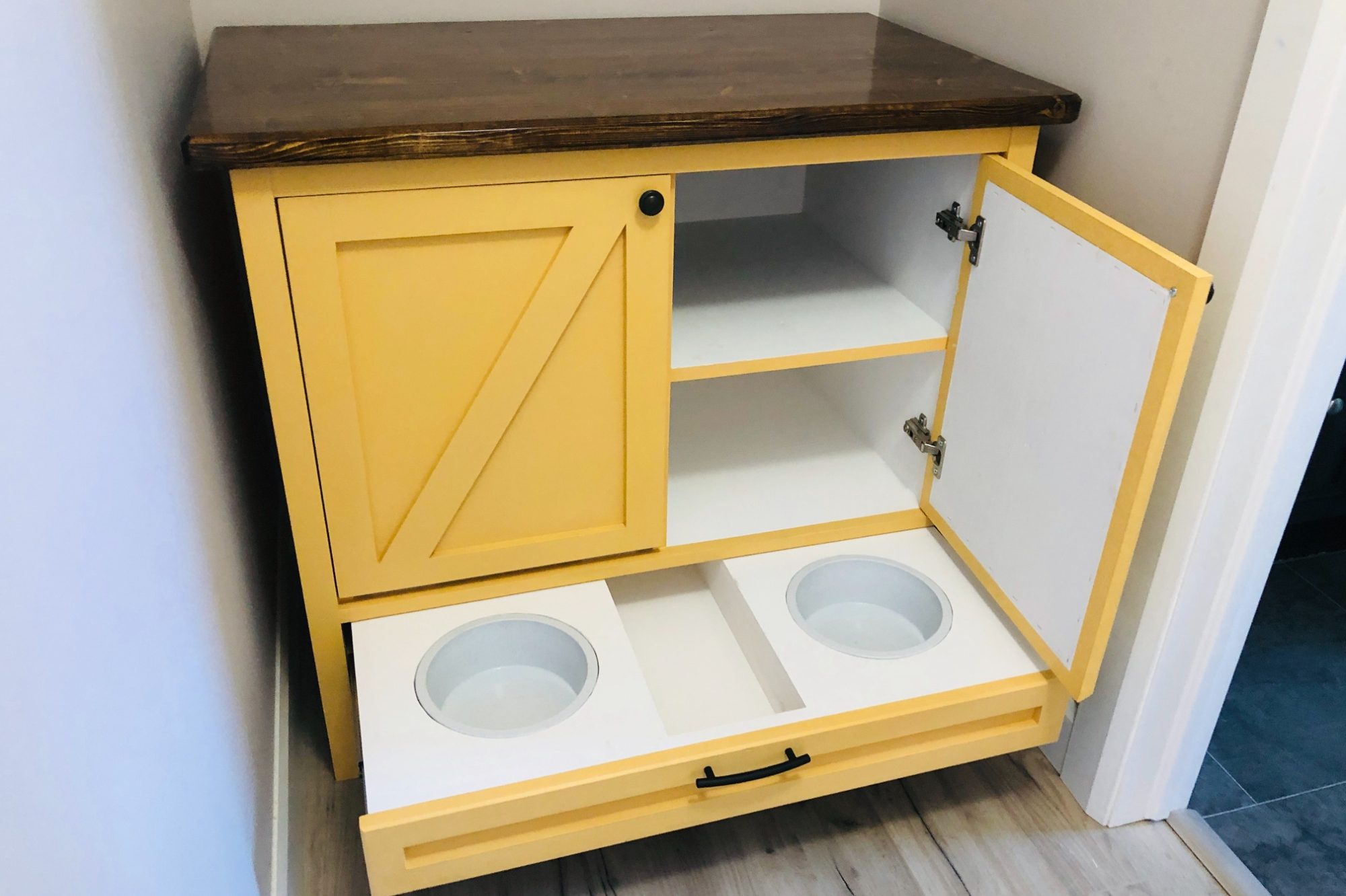Yellow cabinet with open doors, featuring two bowls in a pull-out drawer and shelves inside.