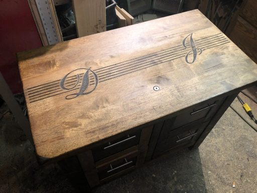 Wooden table with a smooth top and decorative initials "D" and "J" engraved on it.