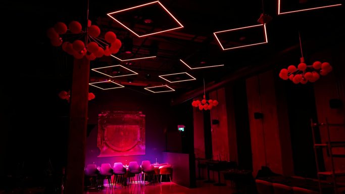 Dimly lit venue with red lighting, featuring decorative chandeliers and modern ceiling designs.