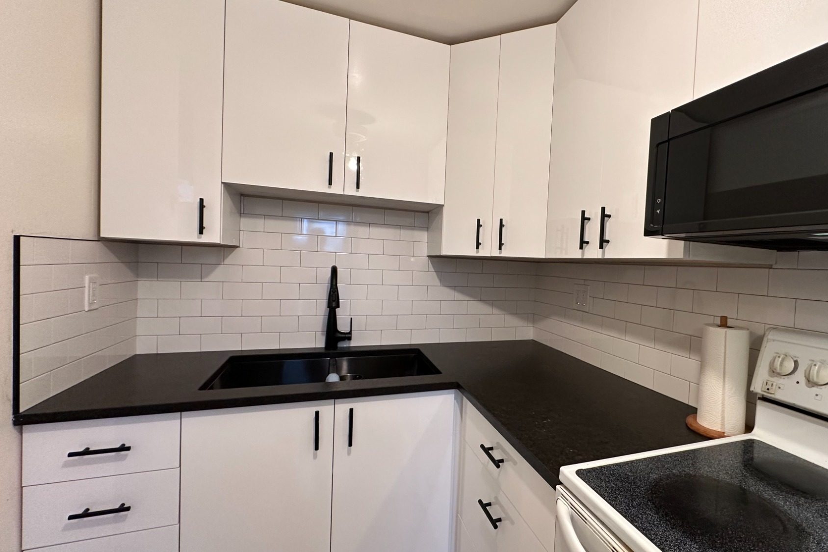 Modern kitchen with white cabinets, black countertops, and stainless steel appliances.